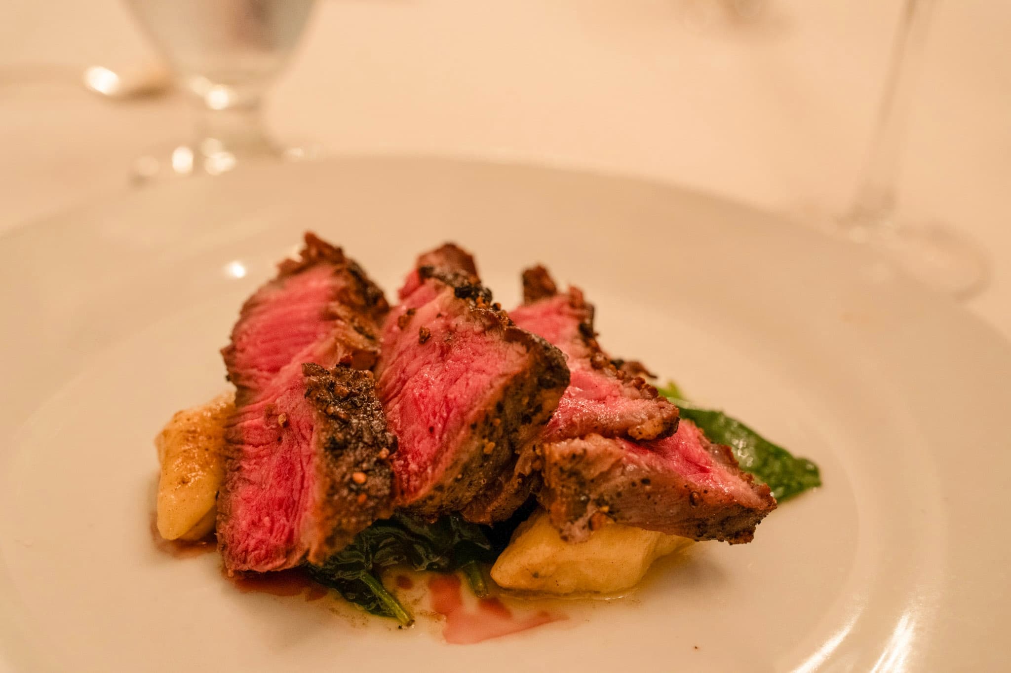 Sliced, medium-rare beef served on a bed of greens and accompanied by gnocchi.