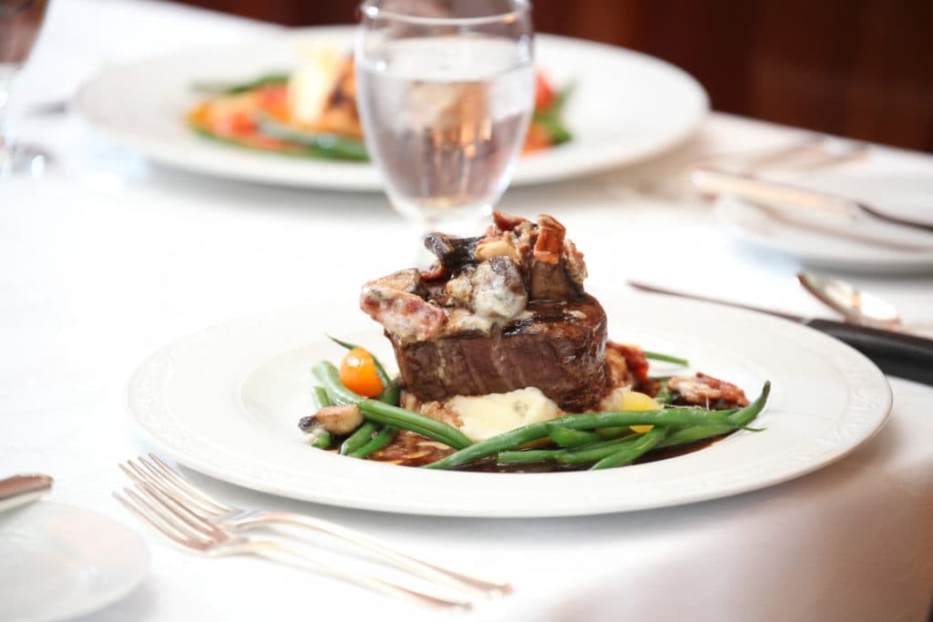 A plated gourmet meal featuring beef, green beans, and a small garnish of vegetables.