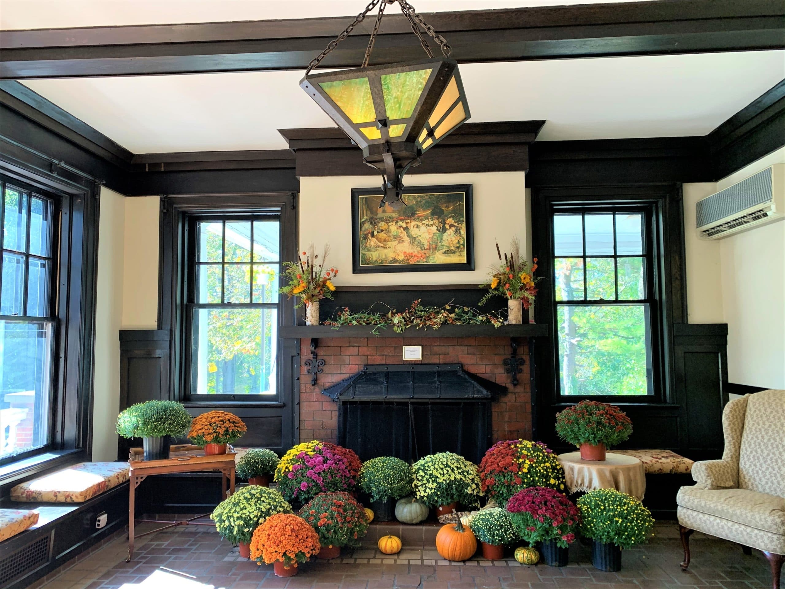 A cozy living room decorated with colorful chrysanthemums and pumpkins near a brick fireplace.