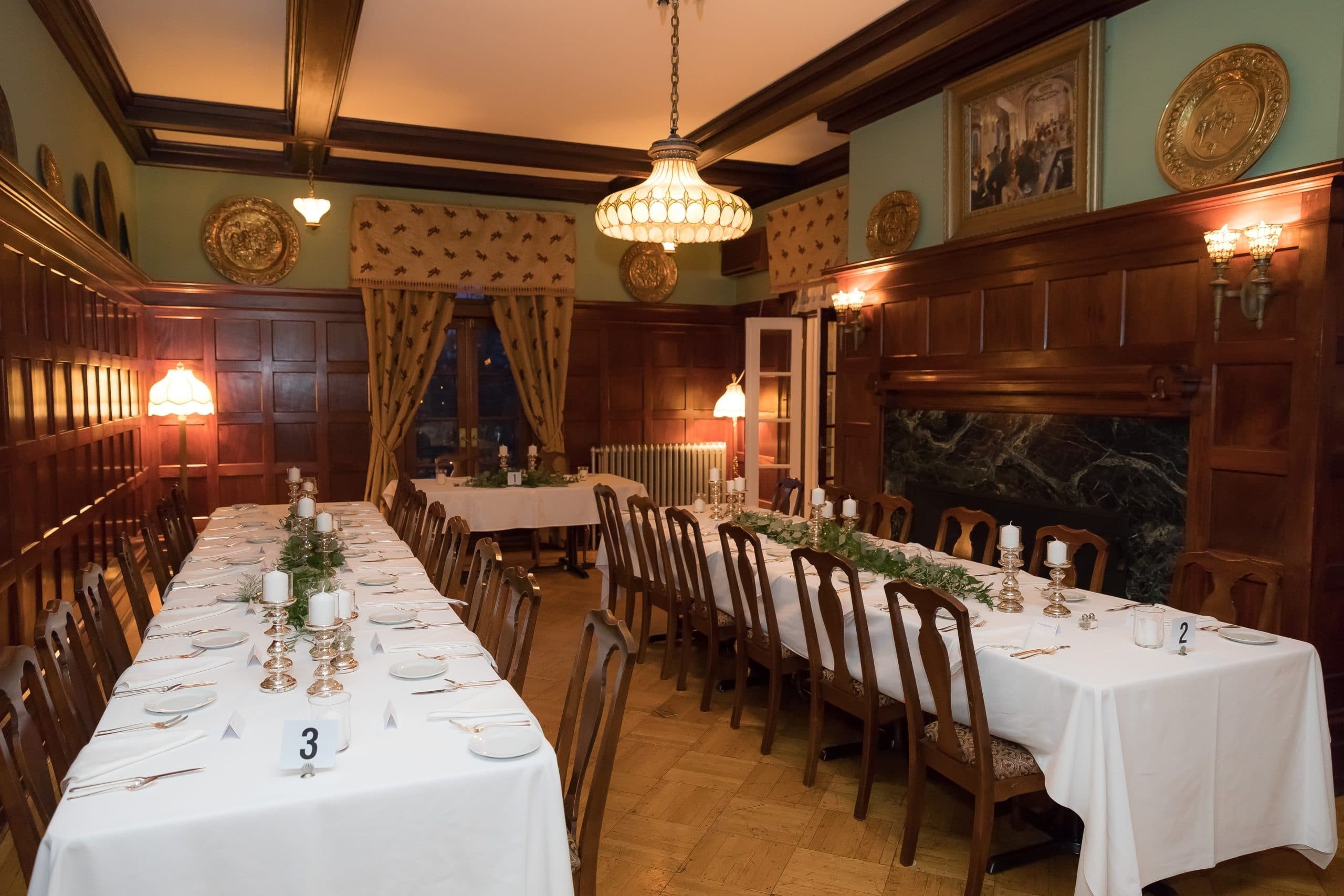 A beautifully set dining room featuring two long tables, elegant decor, and warm lighting.