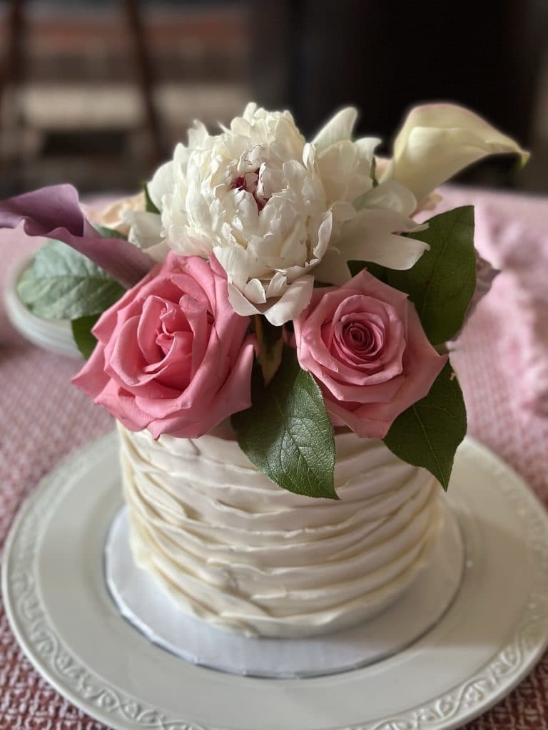 A decorated cake topped with pink roses, a peony, and greenery.
