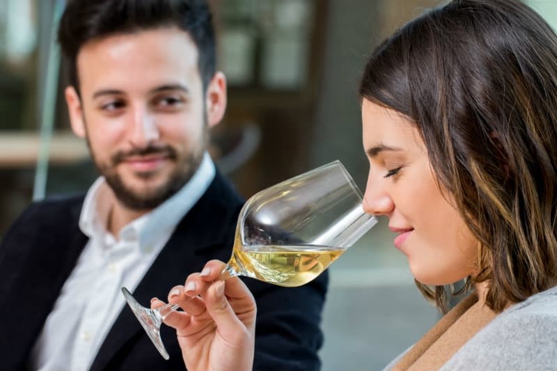 A woman enjoys a glass of wine while a man gazes at her admiringly.