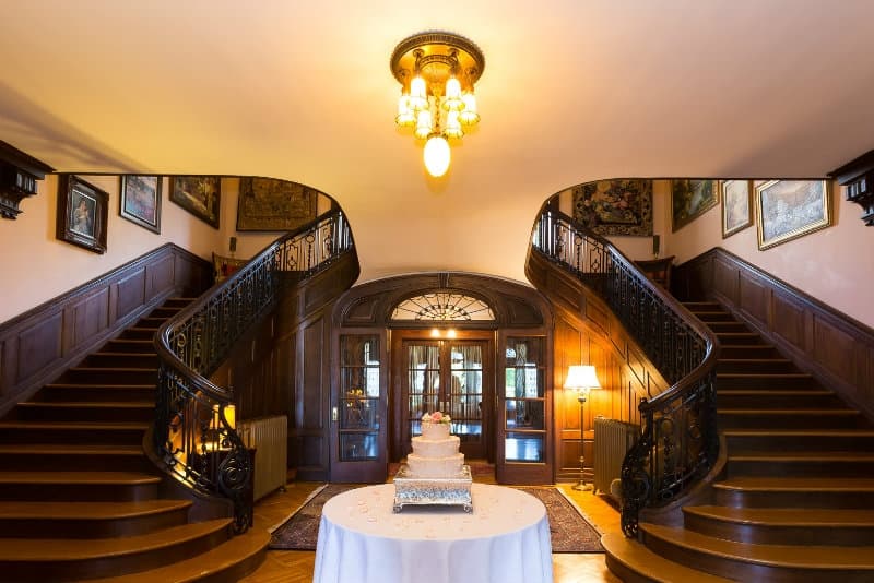 A grand entryway features a double staircase flanking a table with a wedding cake.