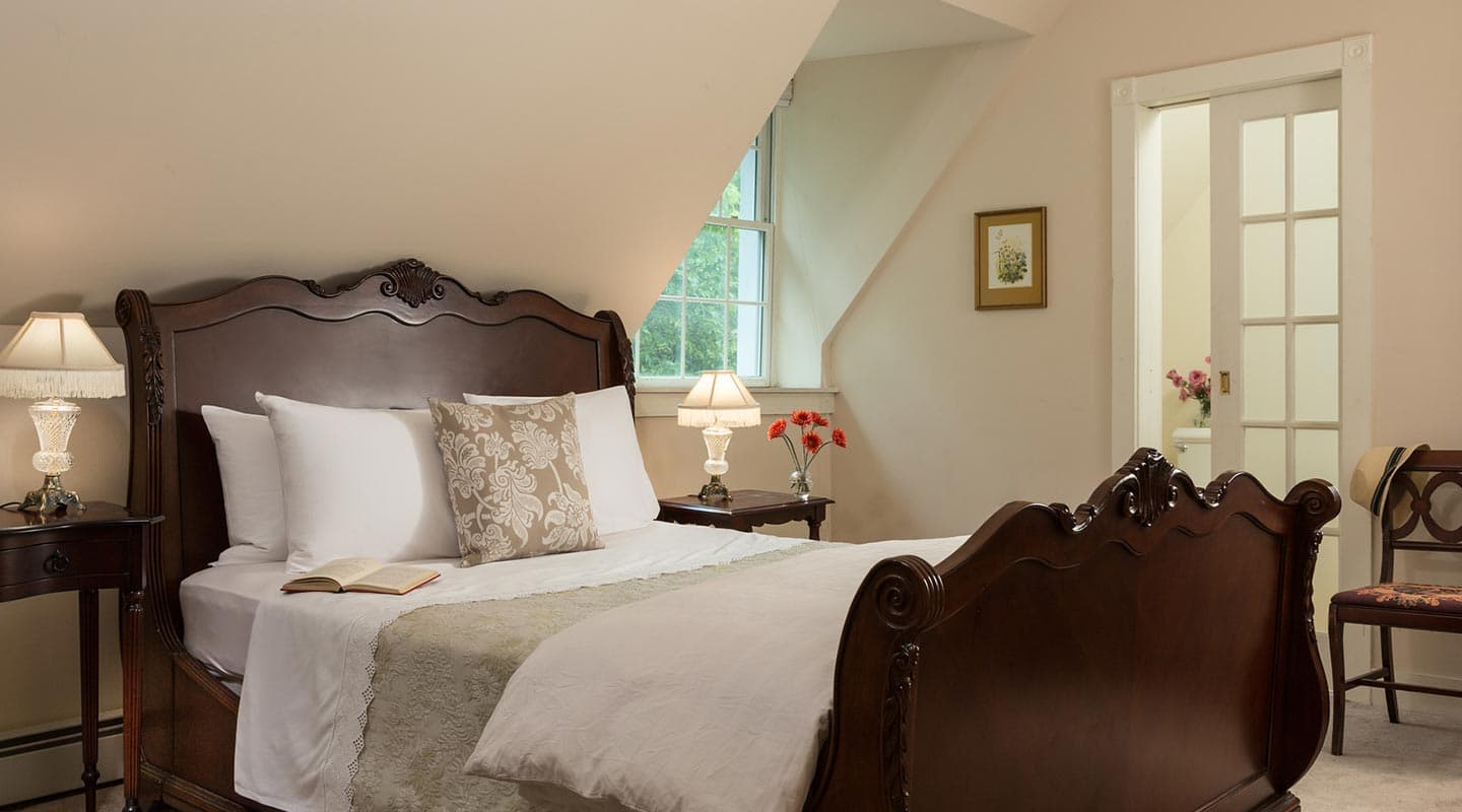A cozy bedroom featuring a wooden bed, bedside tables with lamps, and a window with natural light.