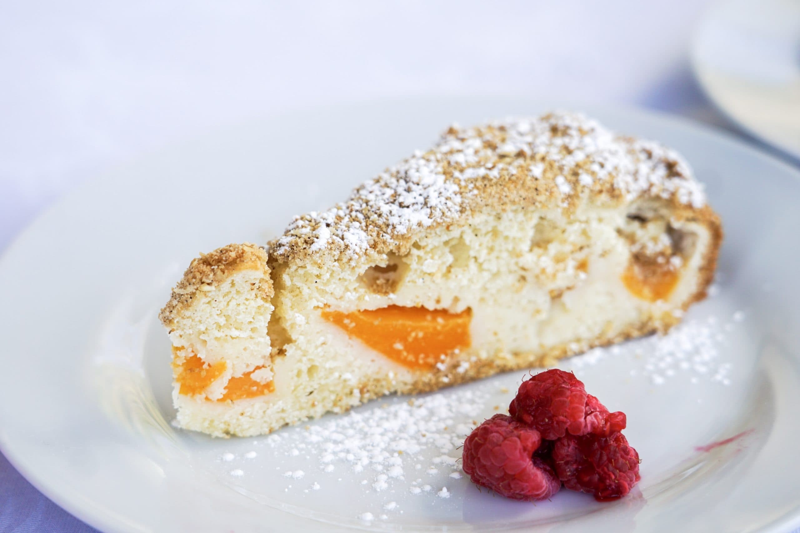 A slice of fruit-filled cake dusted with powdered sugar, accompanied by fresh raspberries.