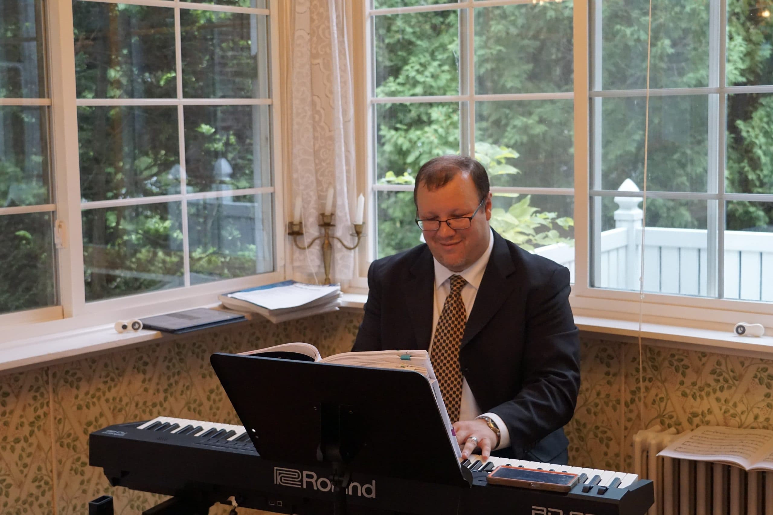 A man in a suit plays a keyboard in a bright room with large windows.