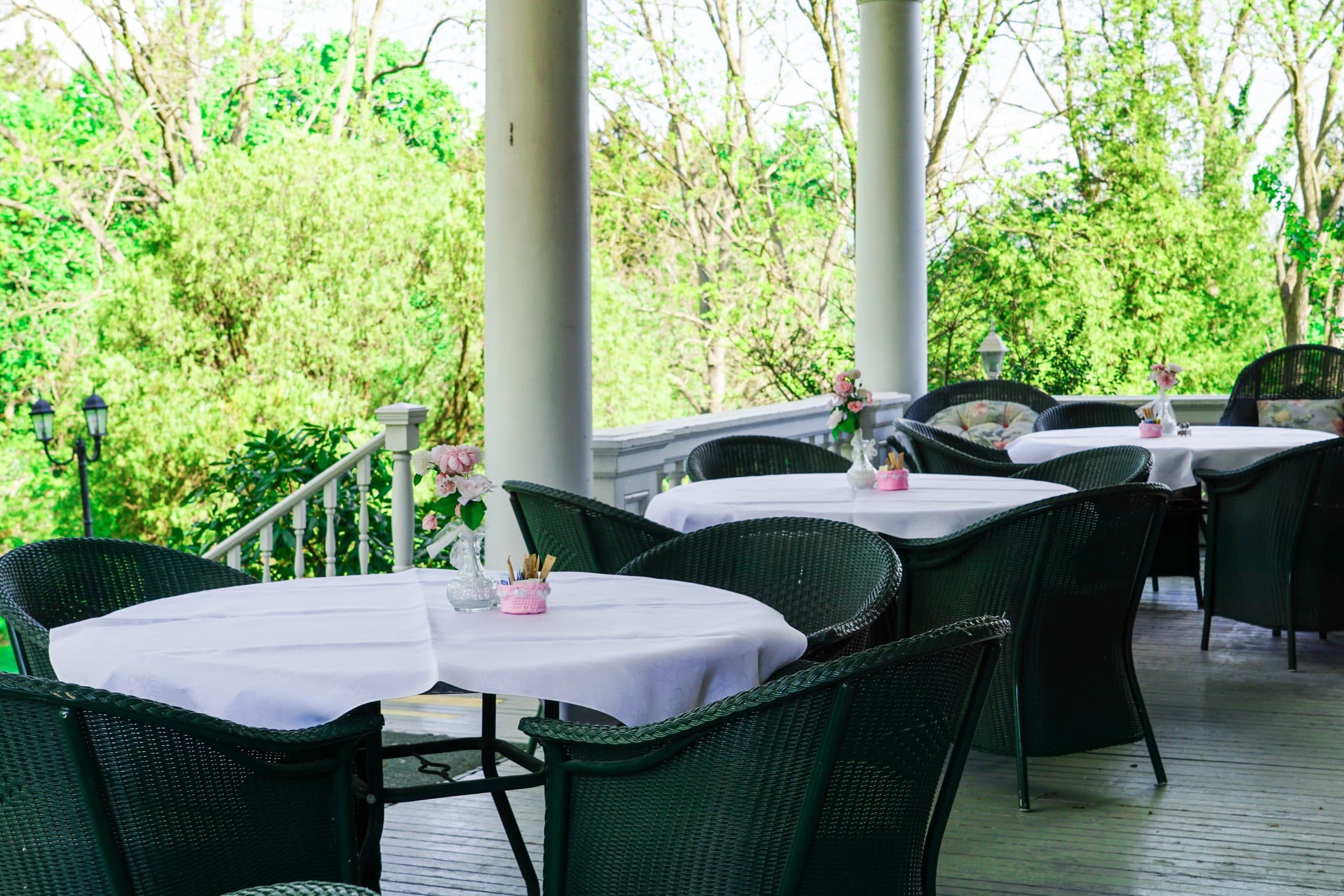 Outdoor dining area with round tables and green wicker chairs, featuring floral centerpieces.