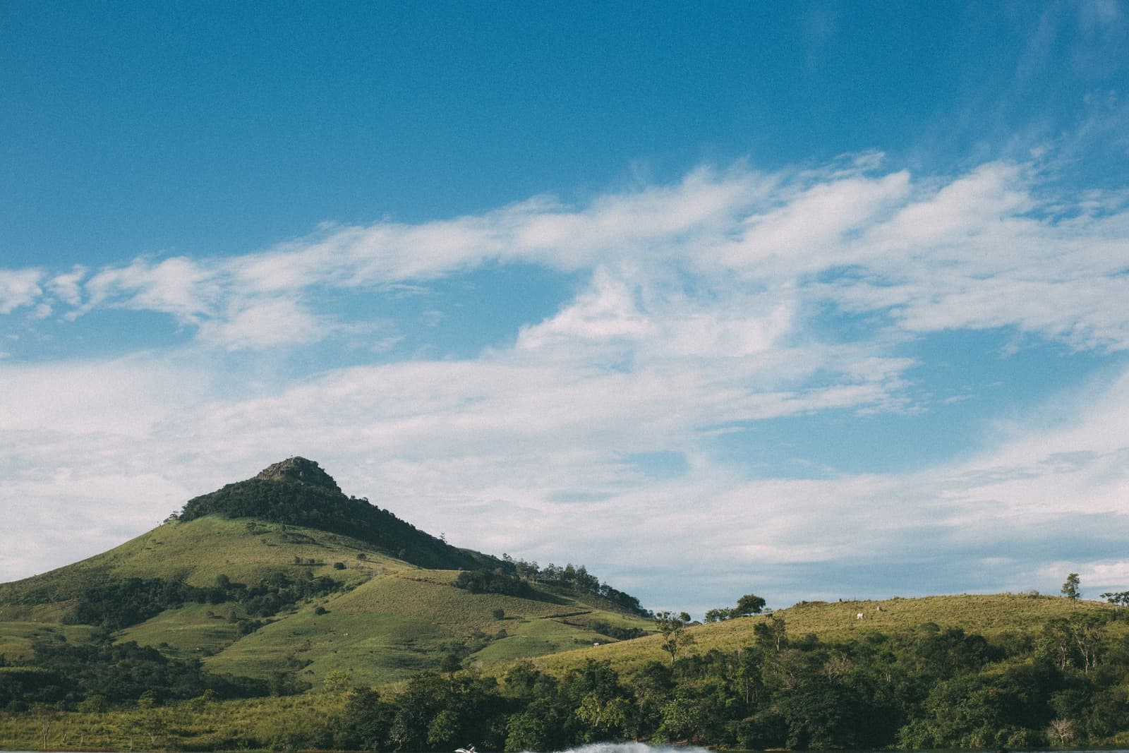 A lush green hill rises under a blue sky with scattered clouds.