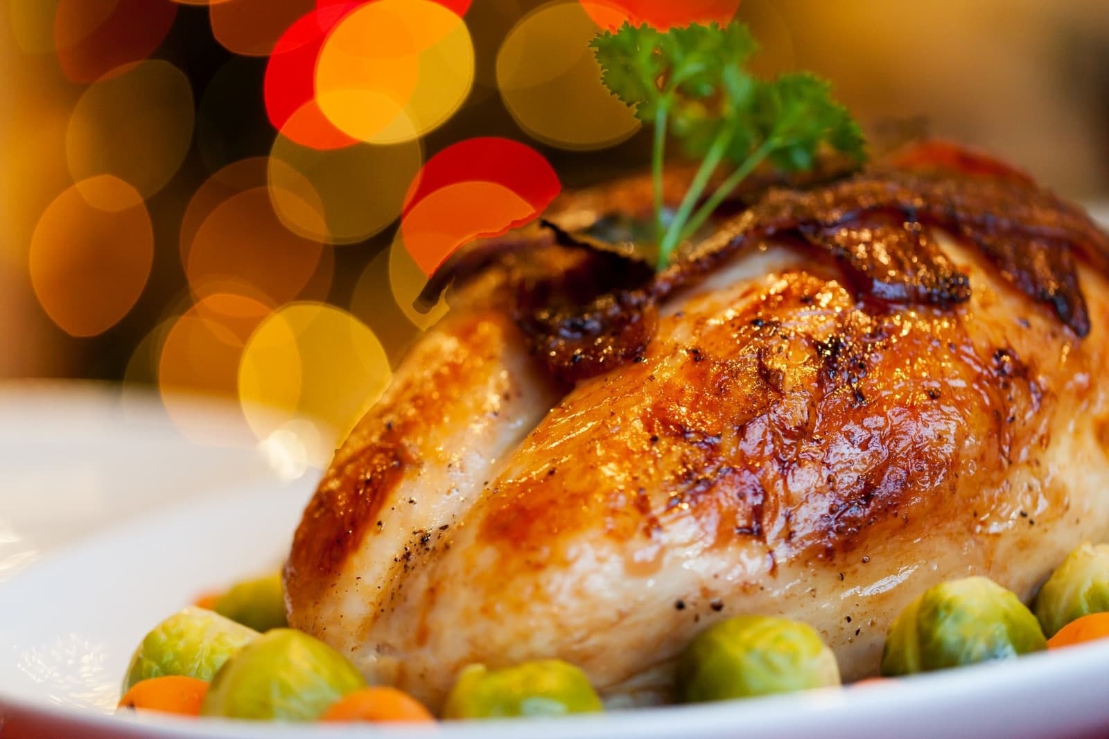 A beautifully roasted turkey with garnishes, surrounded by colorful vegetables on a festive background.