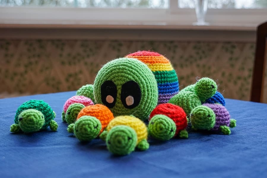 A colorful crocheted octopus surrounded by small crocheted turtles on a blue tablecloth.