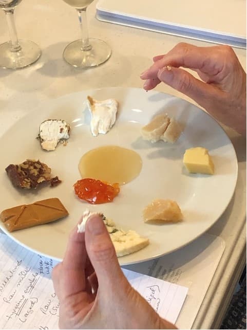 A hand reaches for a piece of cheese on a plate featuring various cheeses and accompaniments.