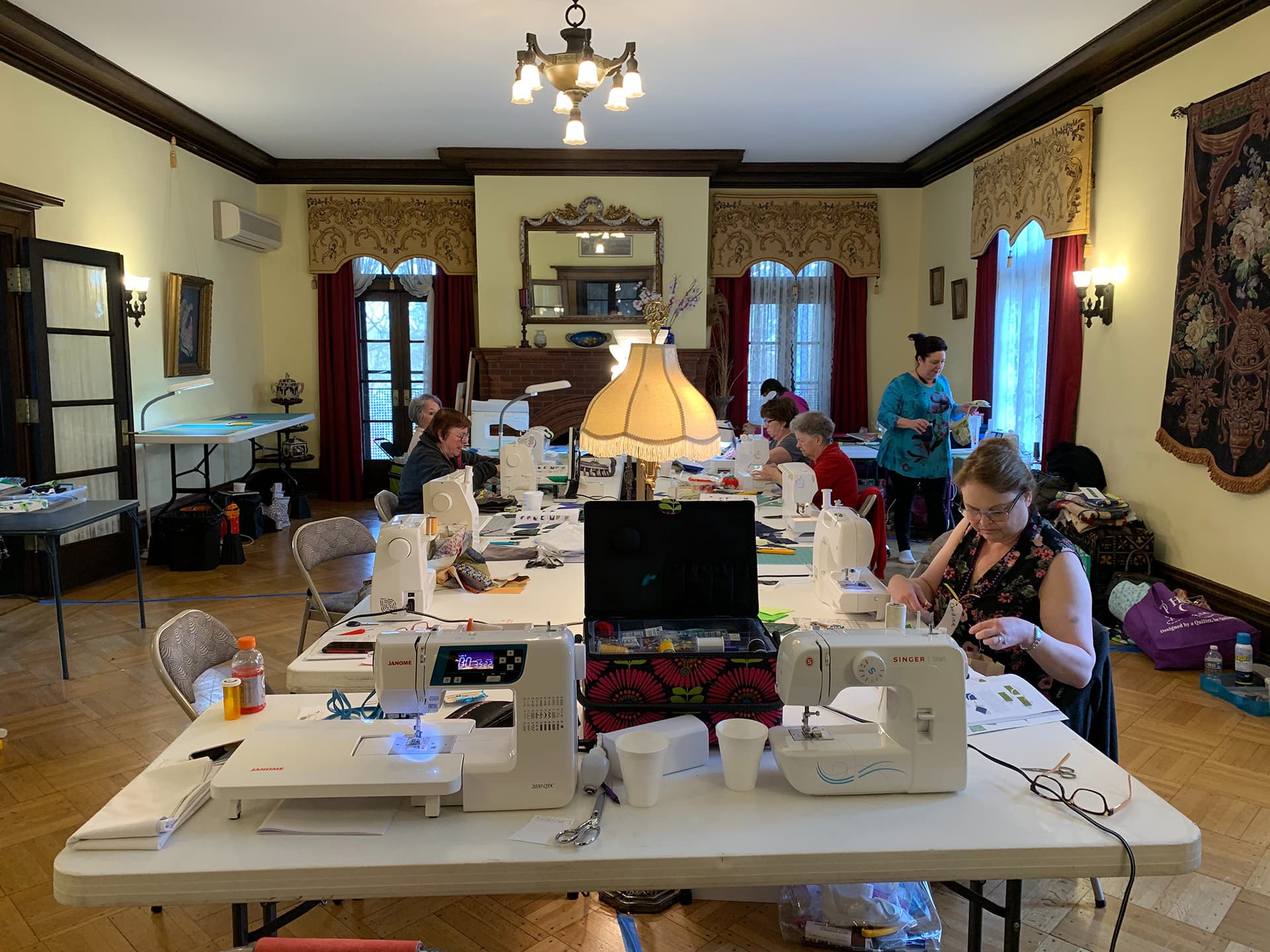 A crafting workshop with several people sewing at tables in a well-lit room.