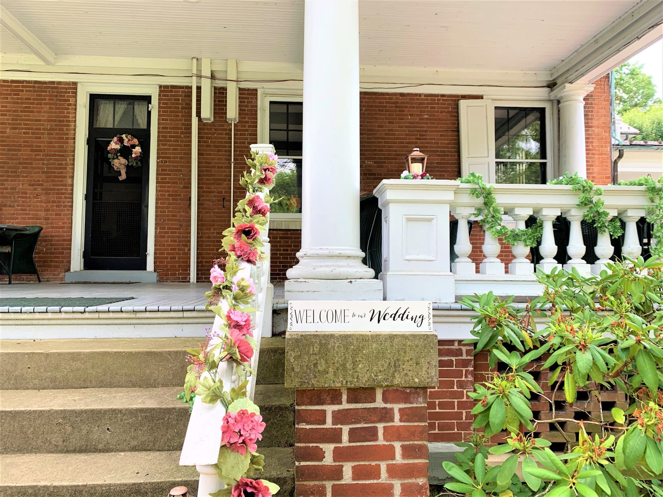 A welcoming porch decorated with flowers and a sign for a wedding event.