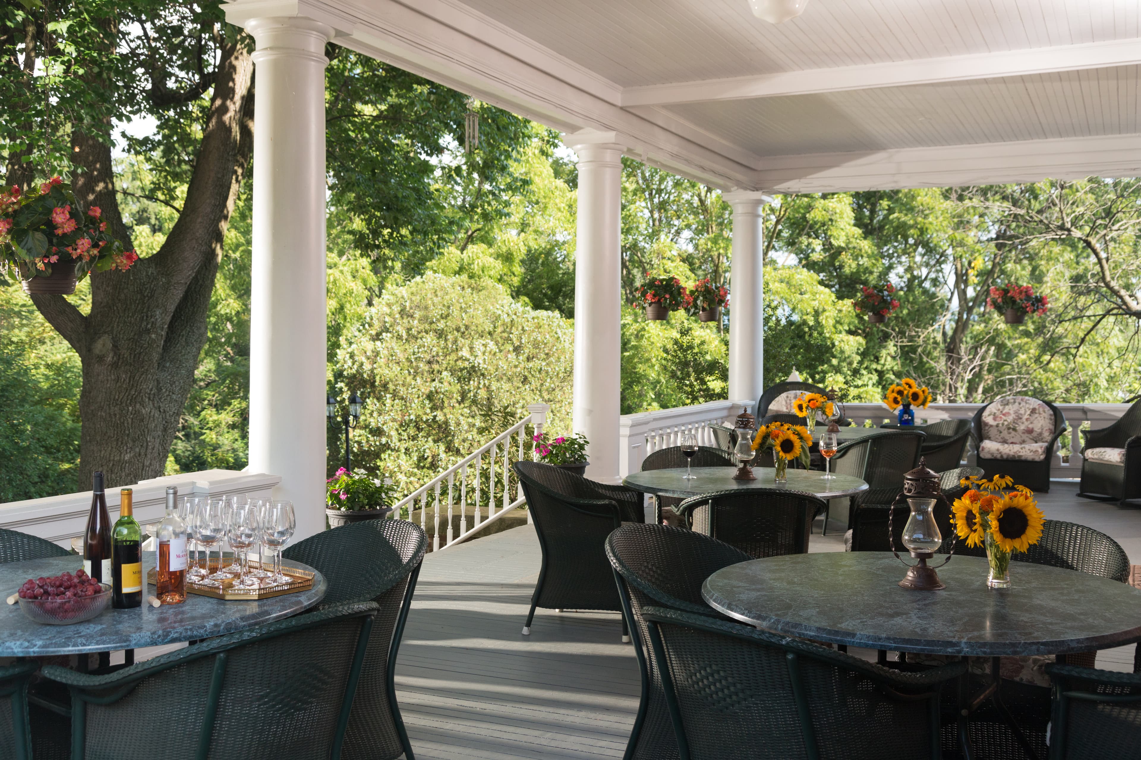 A charming outdoor porch with tables, chairs, and vibrant sunflowers, surrounded by lush greenery.