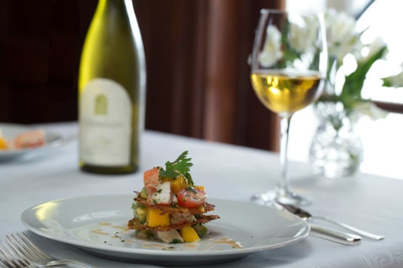 A plate of layered salad garnished with herbs, accompanied by a glass of white wine and a bottle in the background.