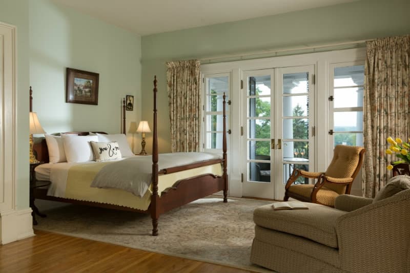 Cozy bedroom featuring a four-poster bed, a sitting area, and large glass doors opening to a scenic view.