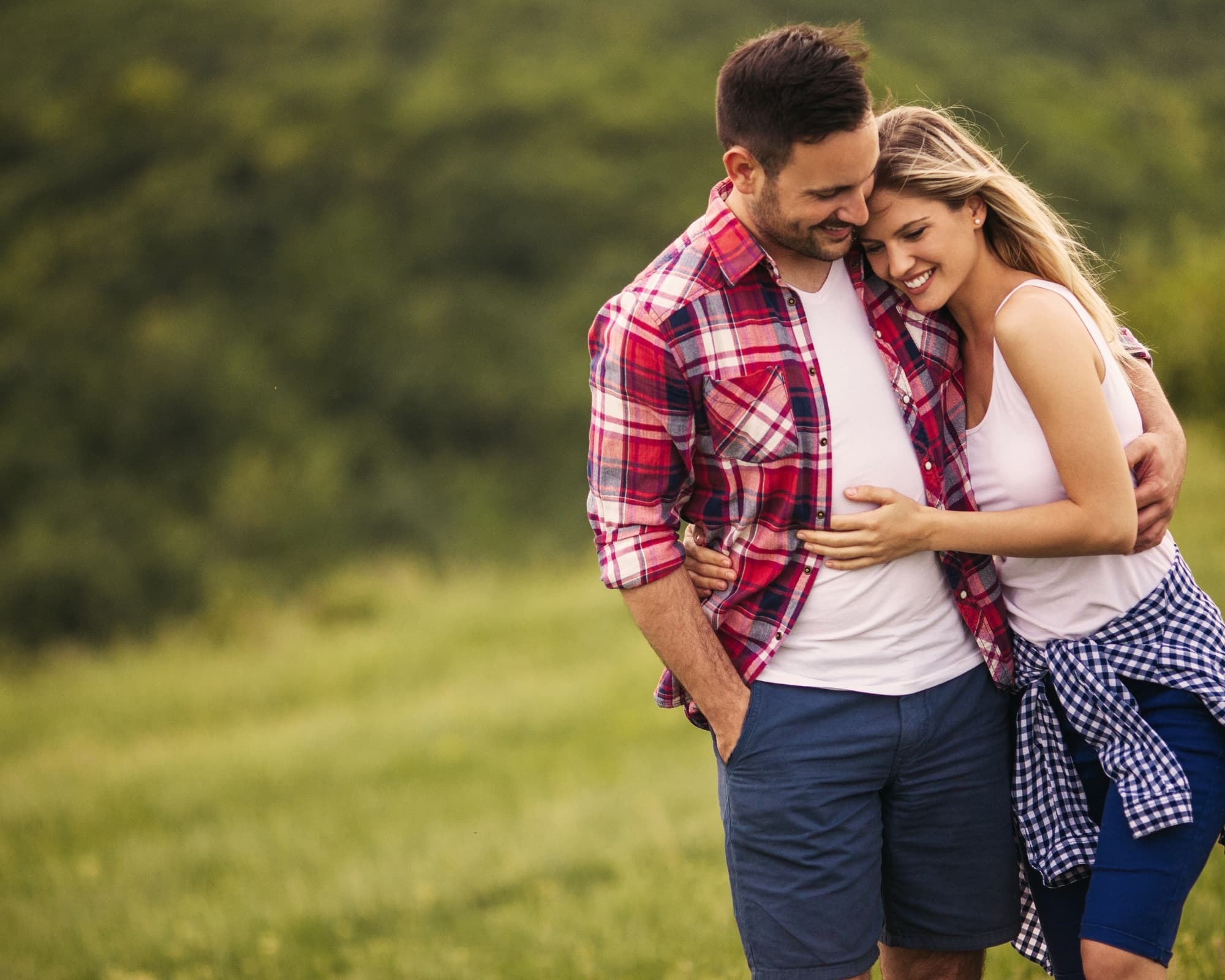 A couple embraces happily in a grassy field.