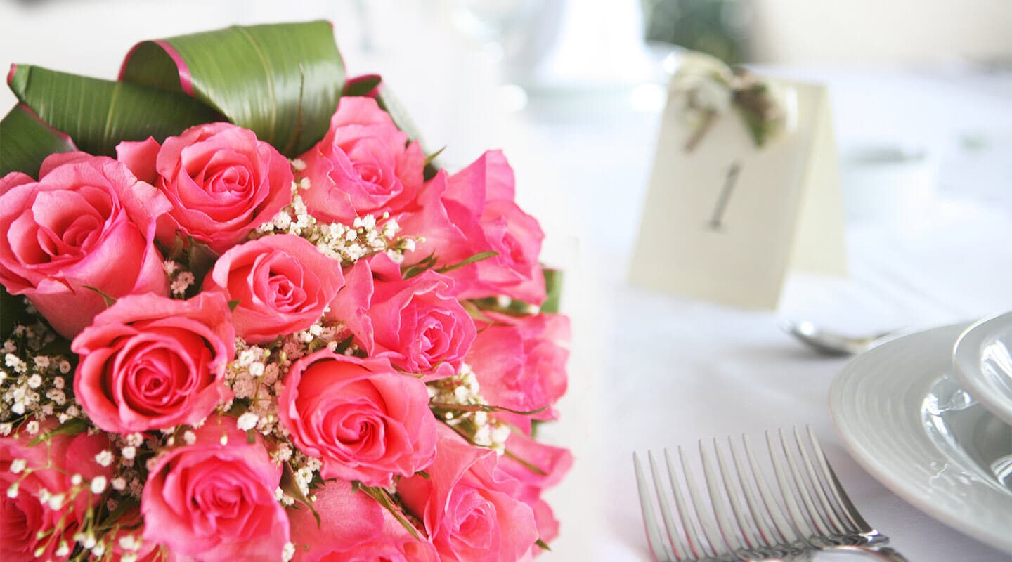 A bouquet of pink roses sits on a table with a place card reading "1."