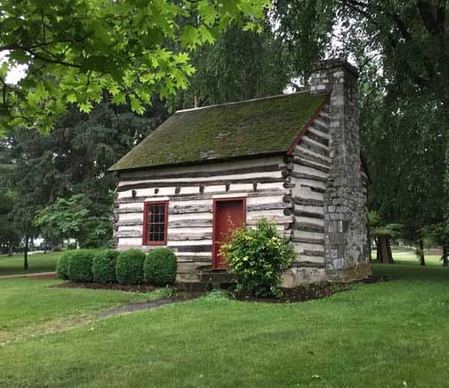 Log cabin with a red door surrounded by greenery.