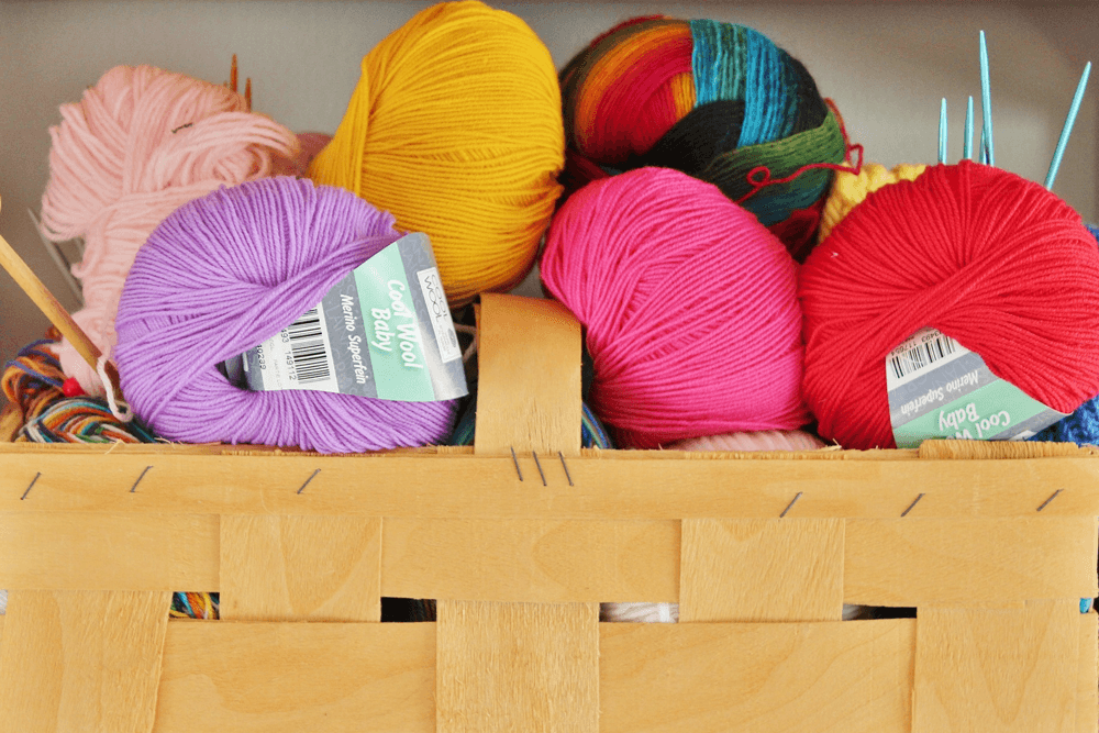 A variety of colorful yarns are stacked in a wooden basket.