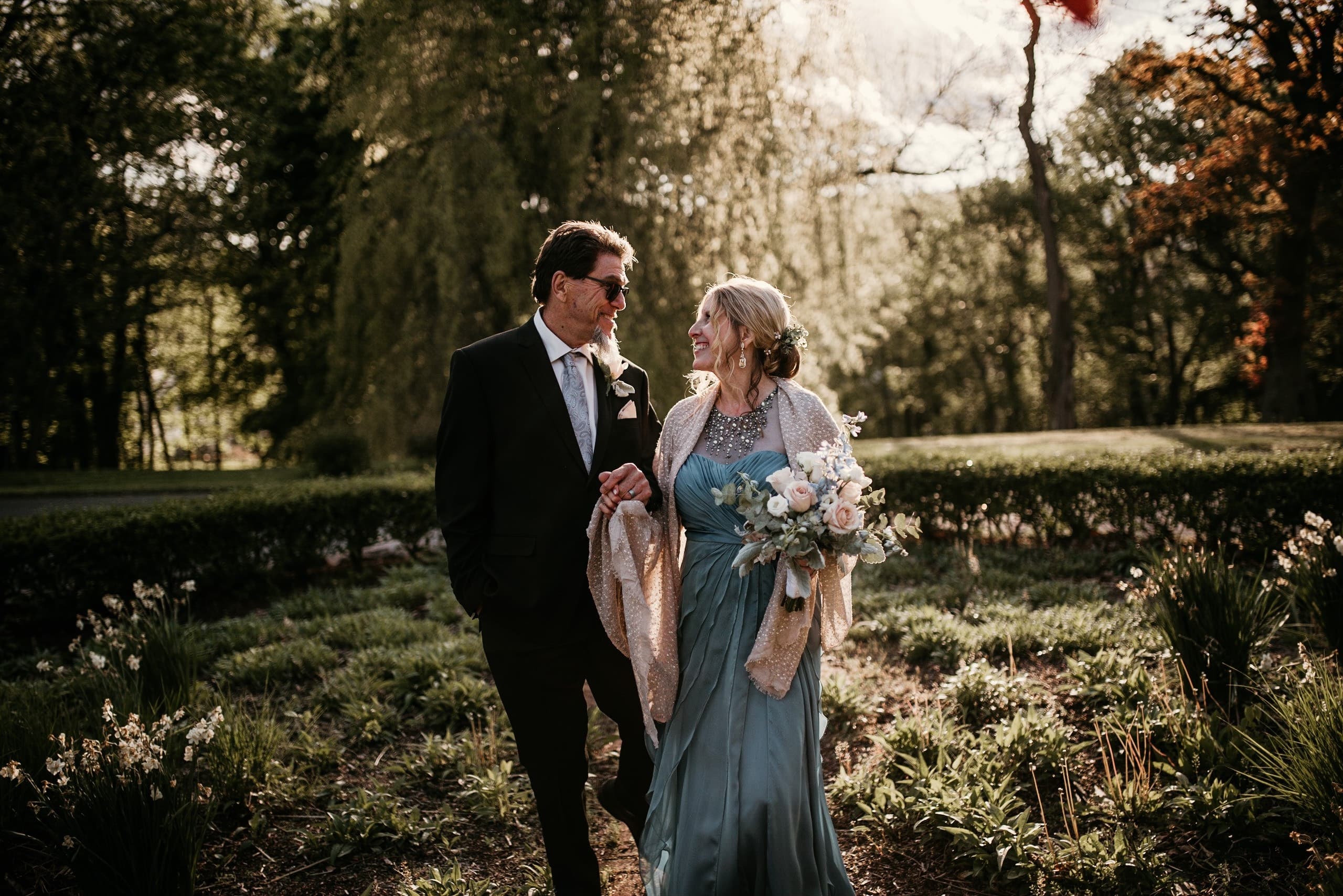 A couple walks hand in hand through a garden, enjoying a sunny day.