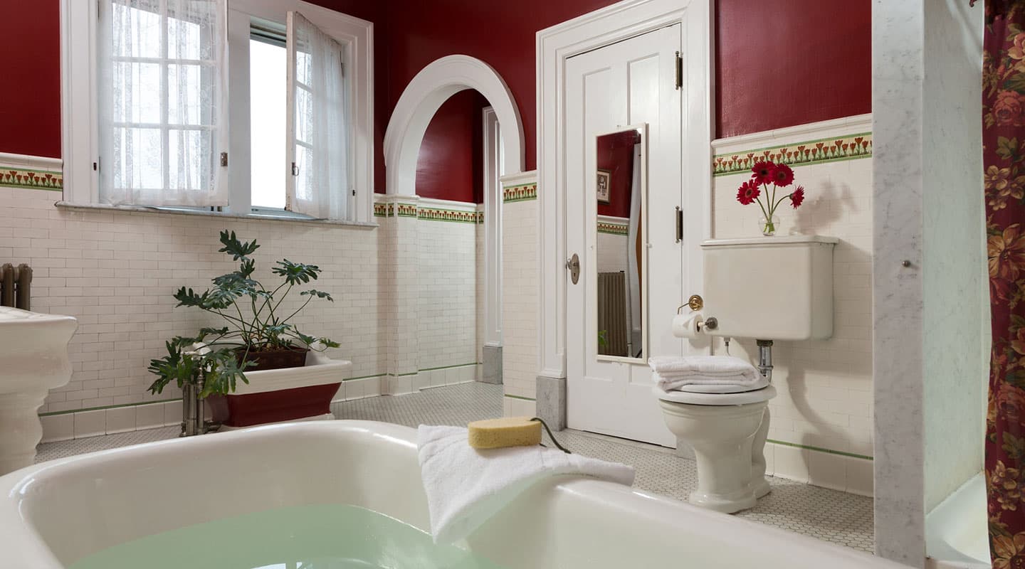 A stylish bathroom featuring a clawfoot tub, red walls, and a potted plant.