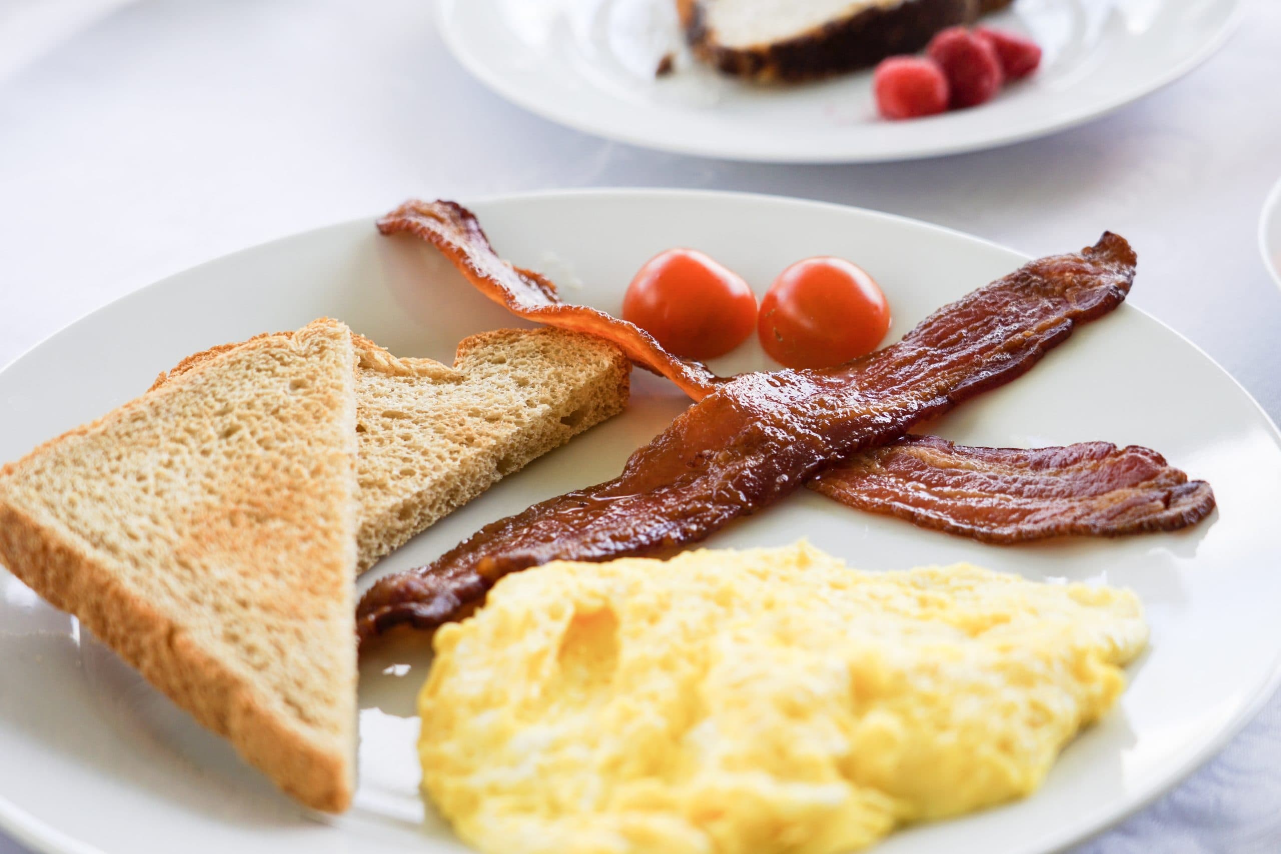 A plate of breakfast featuring scrambled eggs, crispy bacon, toast, and cherry tomatoes.