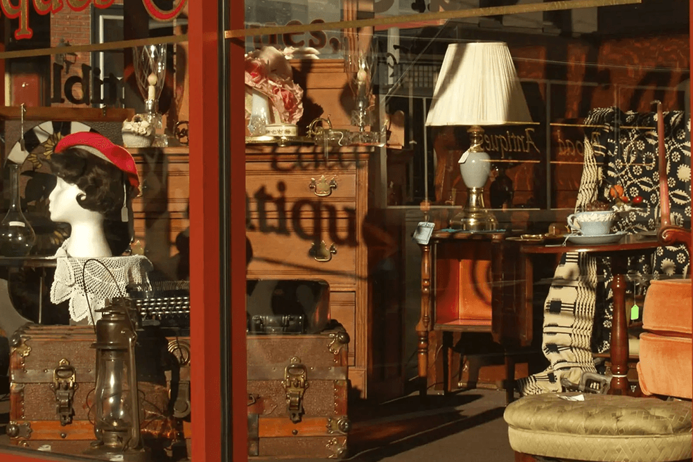 A vintage storefront display featuring a mannequin, antique furniture, and decorative items.