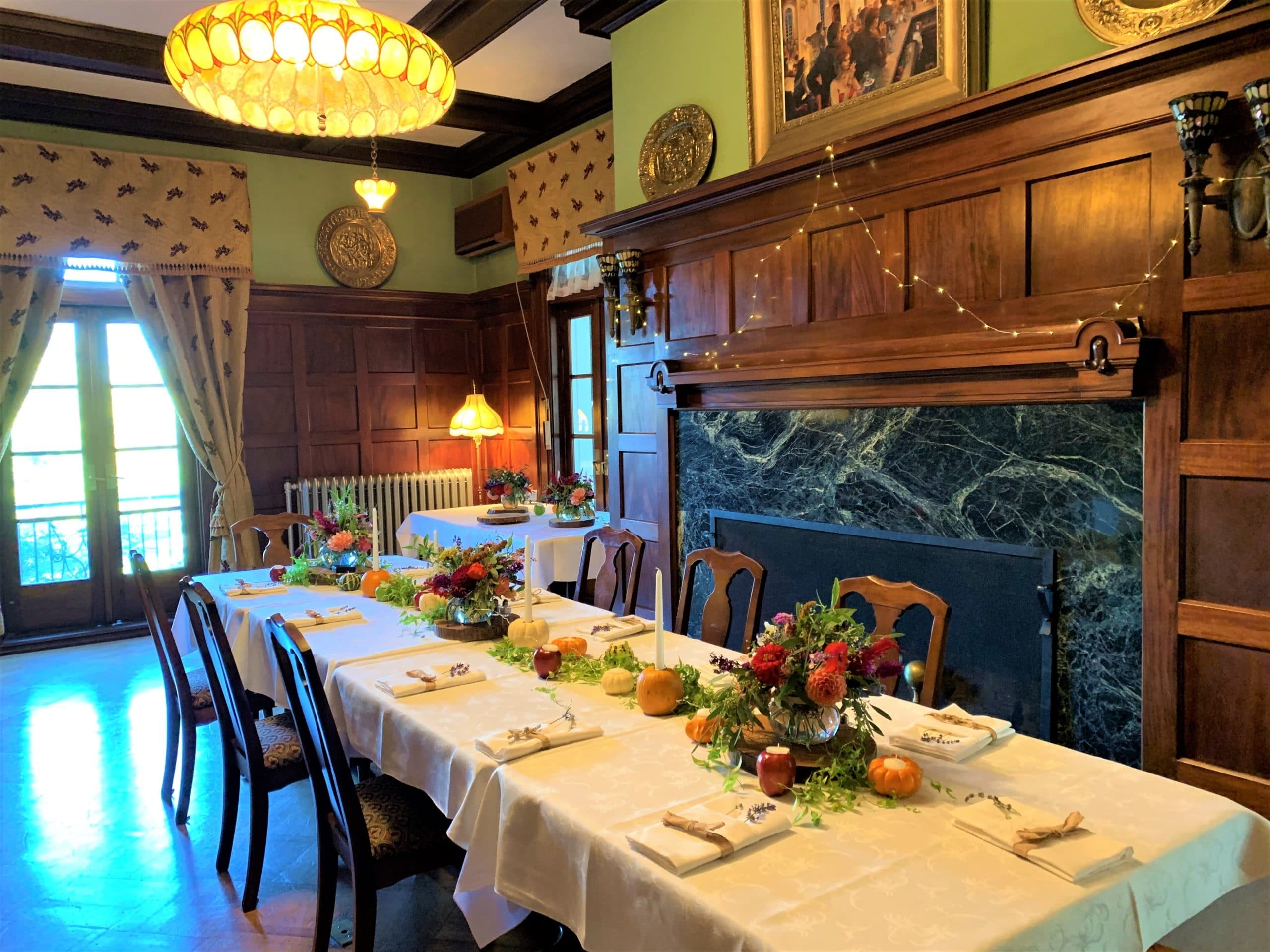 A beautifully set dining table adorned with floral centerpieces in an elegant room featuring wooden walls and a fireplace.