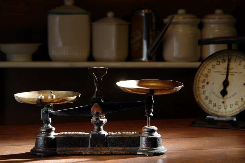 A vintage balance scale with brass pans sits on a wooden table, surrounded by kitchenware.