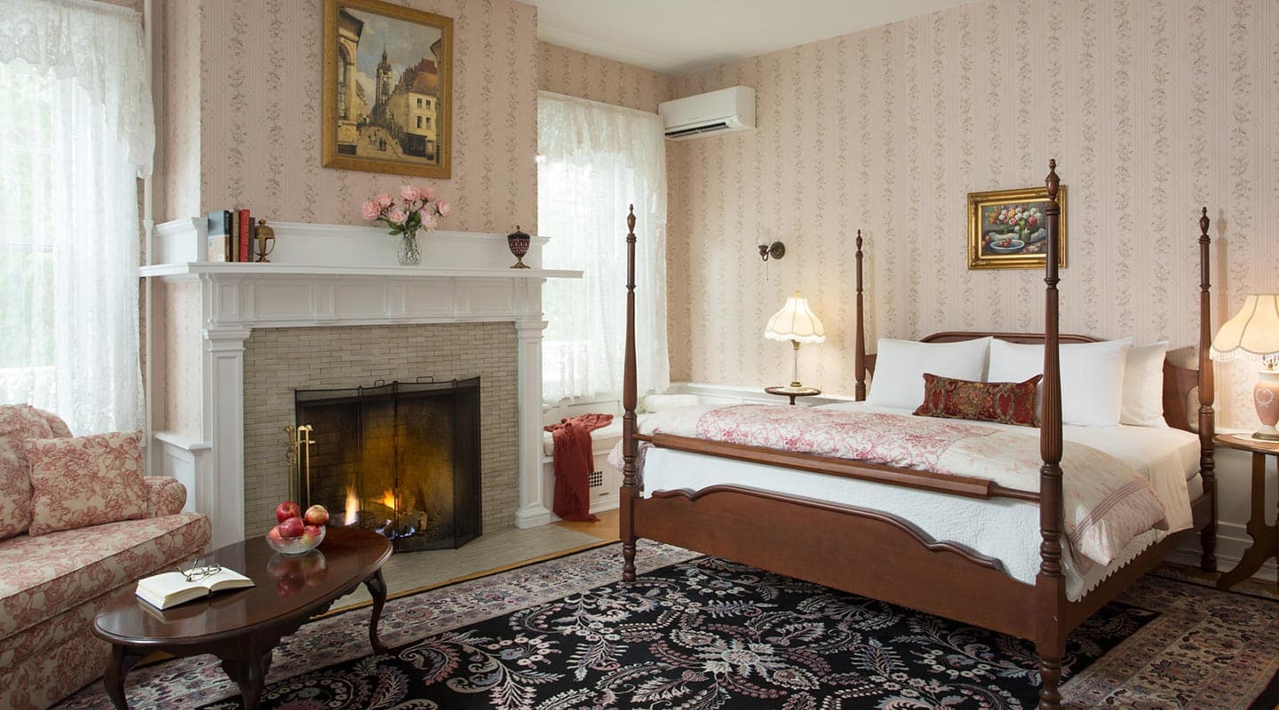 A cozy bedroom featuring a four-poster bed, a fireplace, and floral-patterned decor.