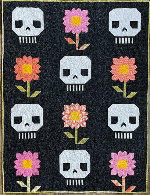 A quilt featuring alternating rows of skulls and colorful flowers on a black background.