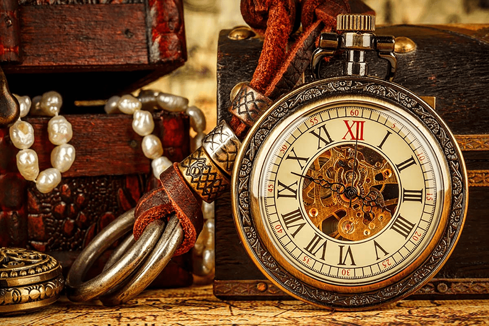 A vintage pocket watch with intricate detailing rests next to ornate wooden boxes and pearl jewelry.