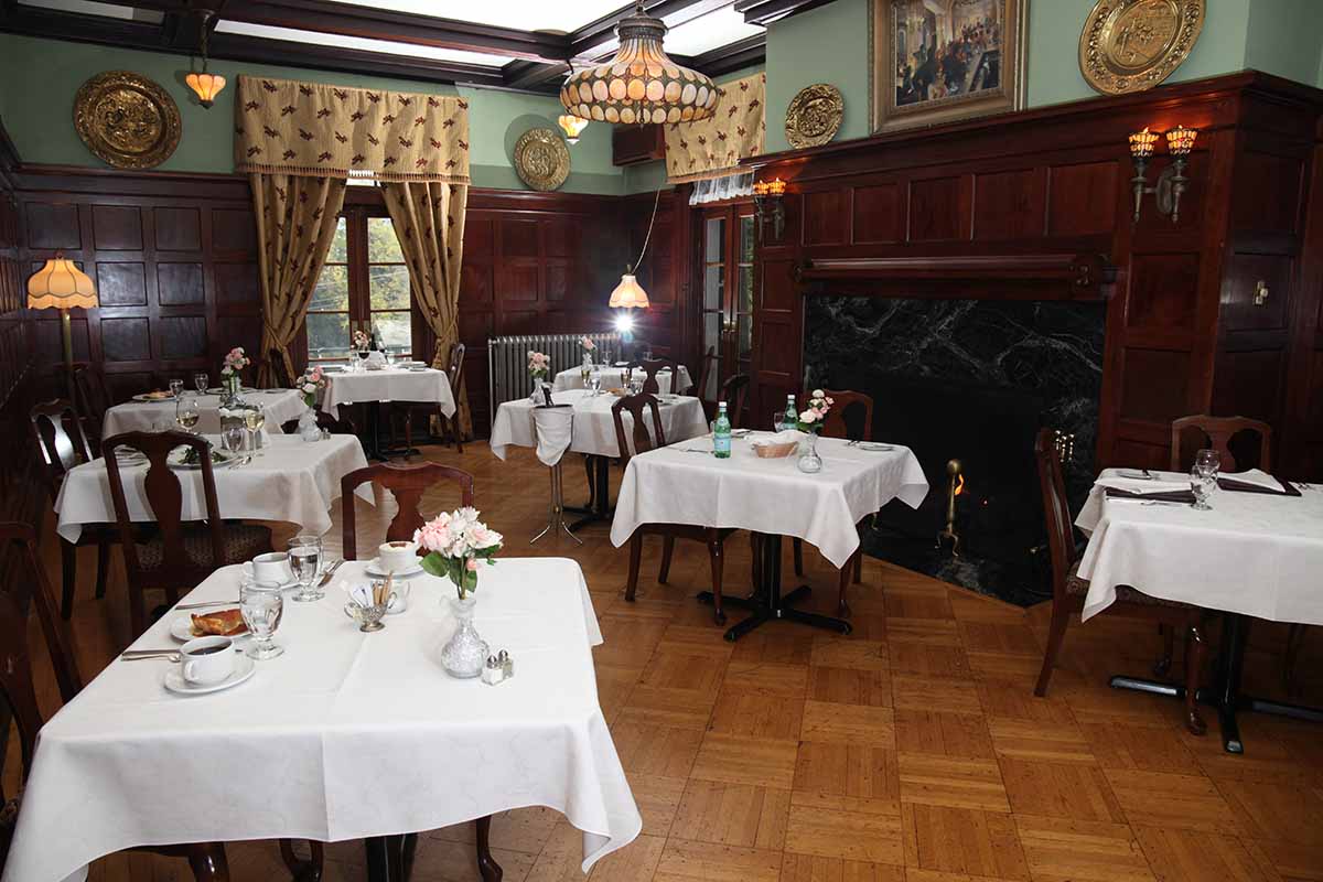 An elegant restaurant interior with tables set for dining, featuring wooden paneling and a fireplace.