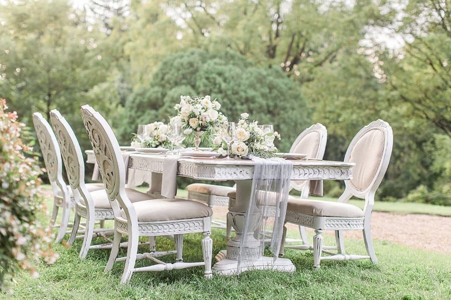 A beautifully arranged outdoor dining table with white chairs and floral centerpieces.