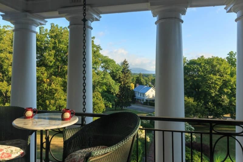 A serene balcony view with two mugs on a round table, surrounded by green trees and distant mountains.
