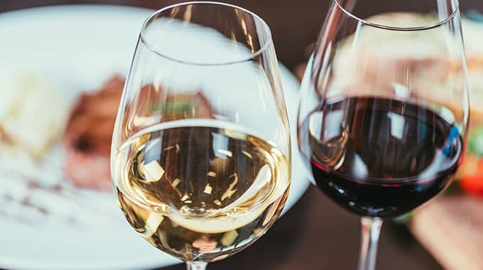 Two wine glasses, one filled with white wine and the other with red, set against a blurred plate of food.