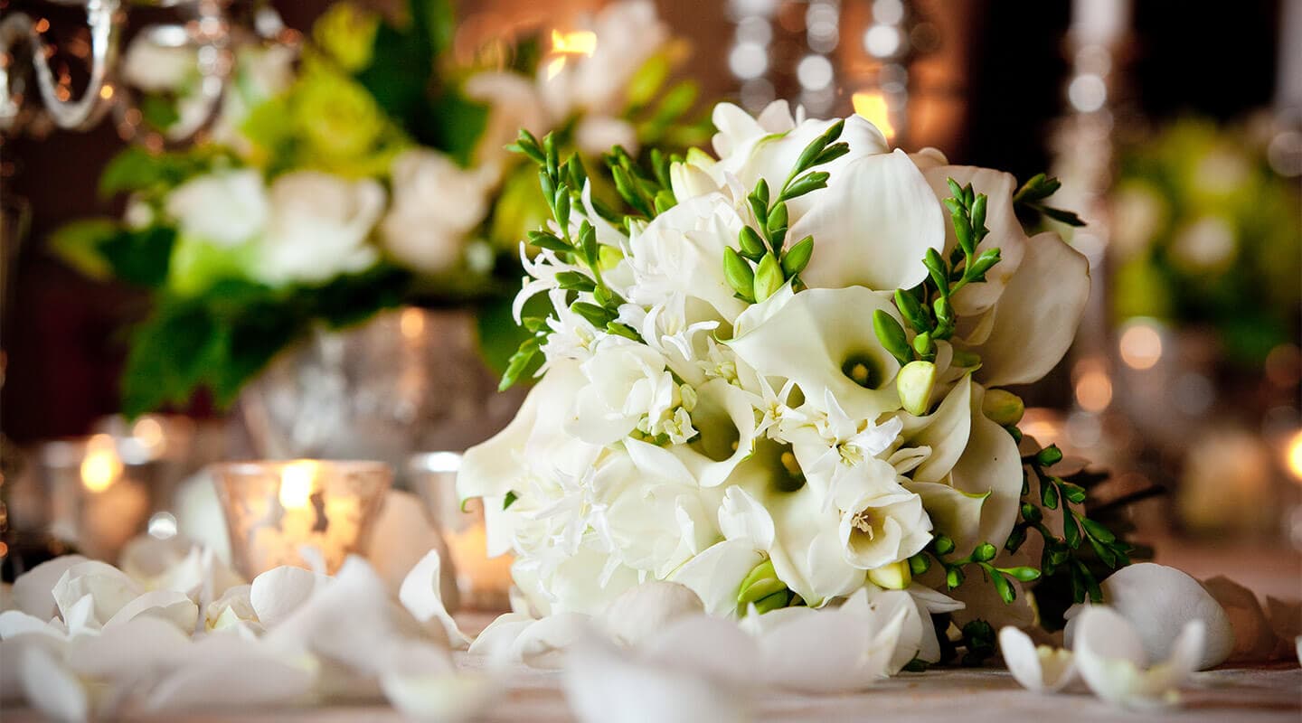 A delicate white floral bouquet lies among scattered petals and softly glowing candles.