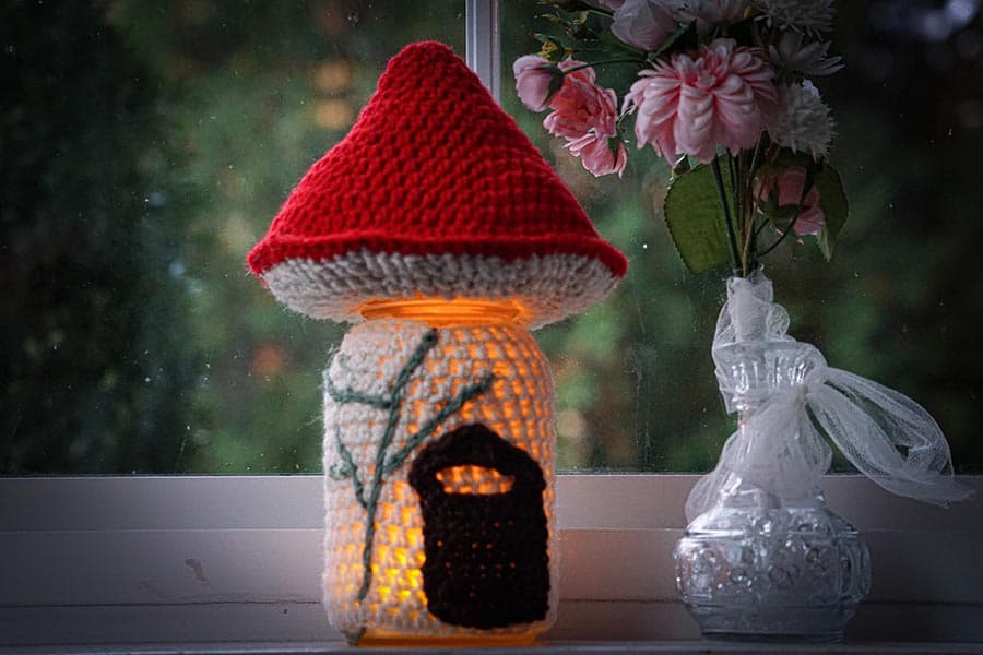 A whimsical lamp with a red mushroom cap design sits on a windowsill next to a vase of flowers.