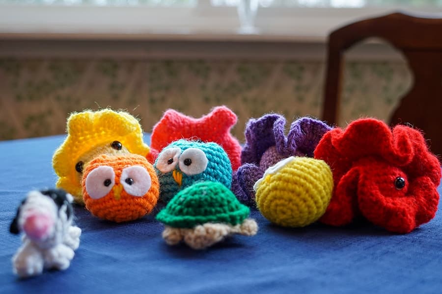 A collection of colorful, crocheted sea creatures and a small white dog figurine on a blue tablecloth.