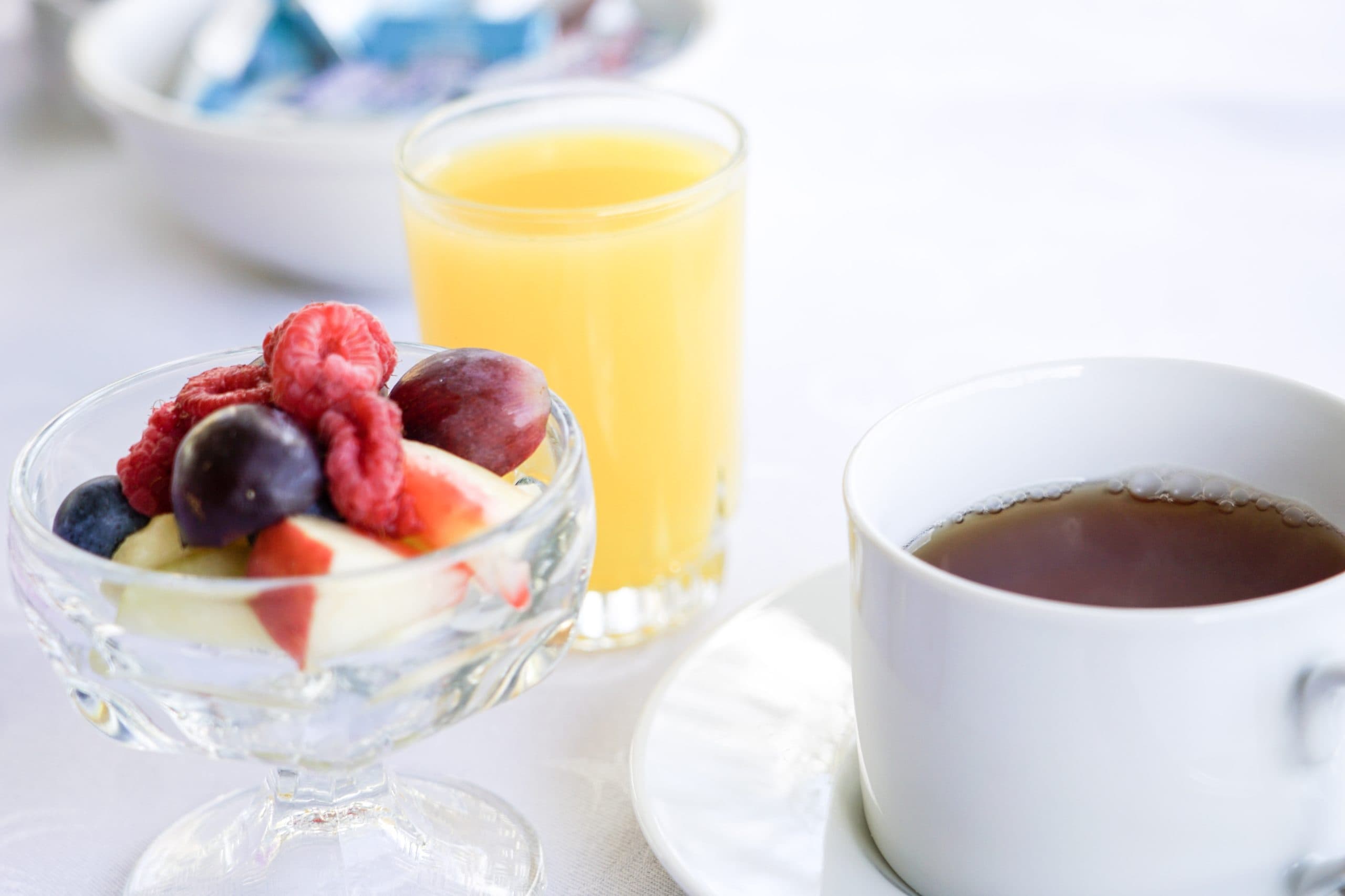 A bowl of mixed fruit, a glass of orange juice, and a cup of tea on a table.