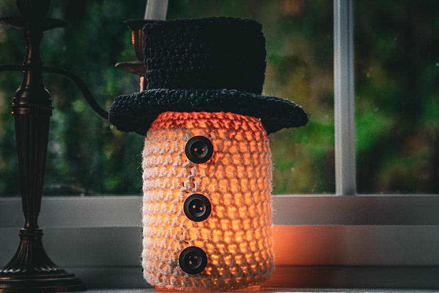 A warm, glowing lamp shaped like a snowman, adorned with a black hat and decorative buttons.