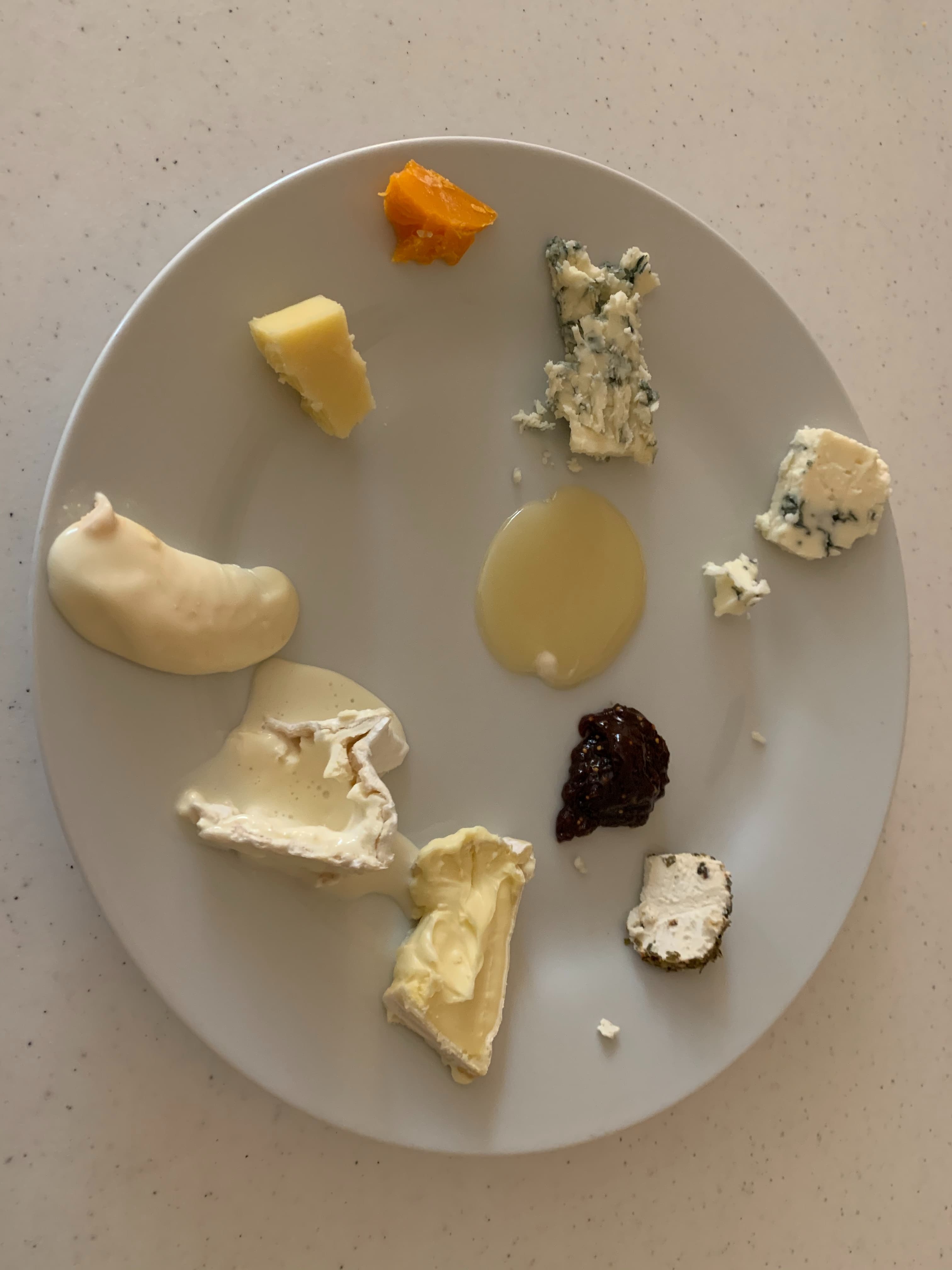 A white plate with a variety of cheeses and accompaniments arranged on it.