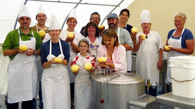 A group of people dressed in aprons and chef hats holds yellow fruits in a kitchen setting.