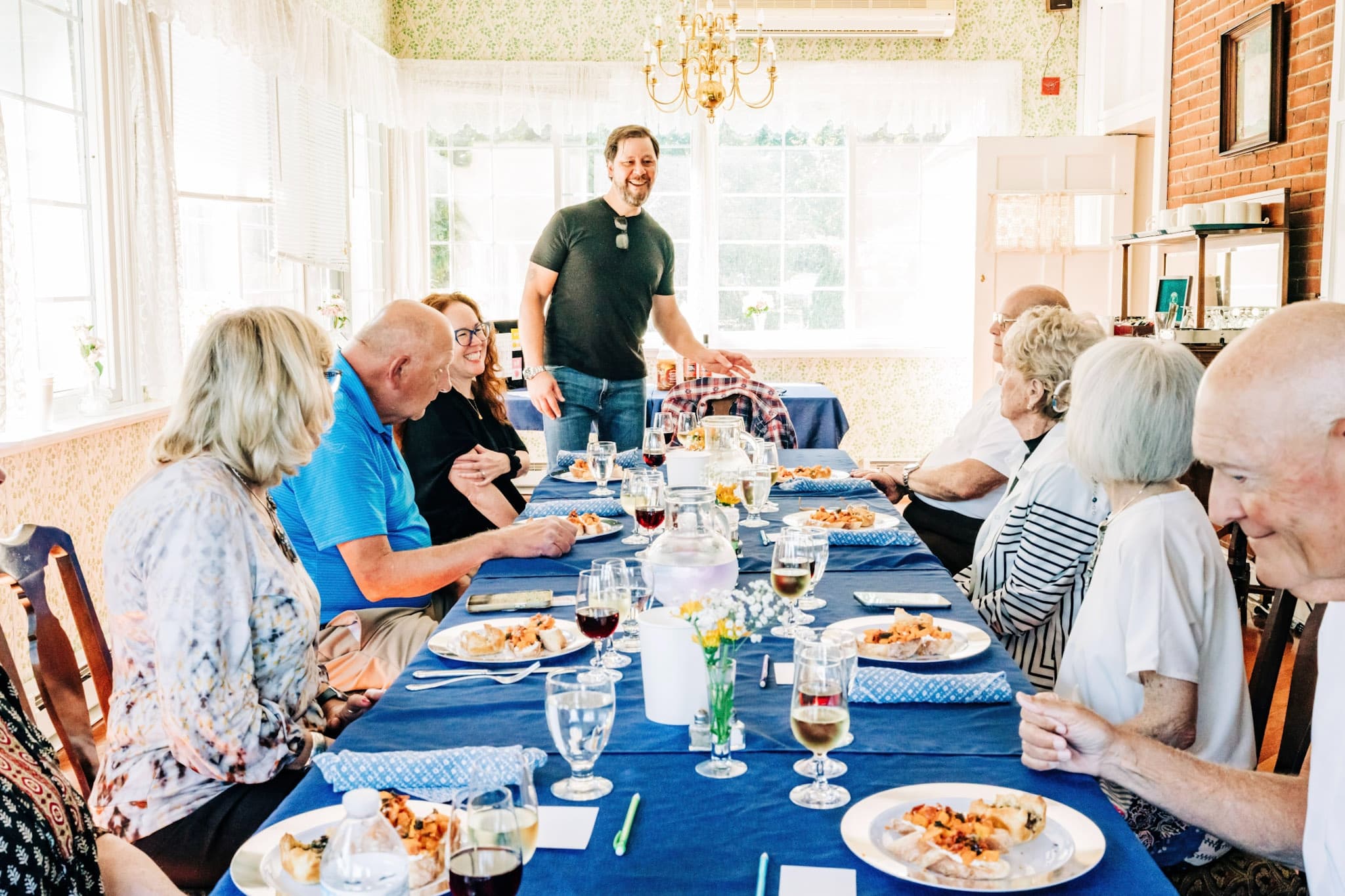 A cheerful gathering of people enjoying a meal around a long table with blue tablecloths.