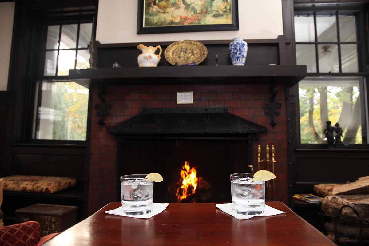 Two drinks sit on a table in front of a cozy fireplace in a warmly decorated room.
