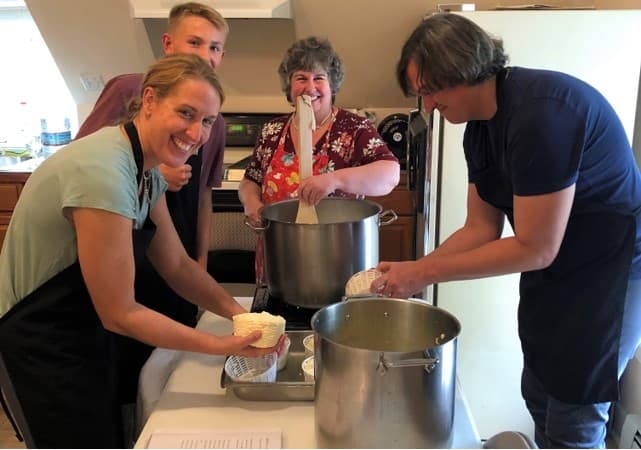 A group of four people smiles while making cheese in a kitchen.