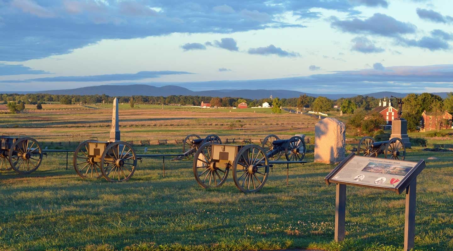 A scenic view of cannons and a historical marker in a grassy battlefield with a distant mountain backdrop.