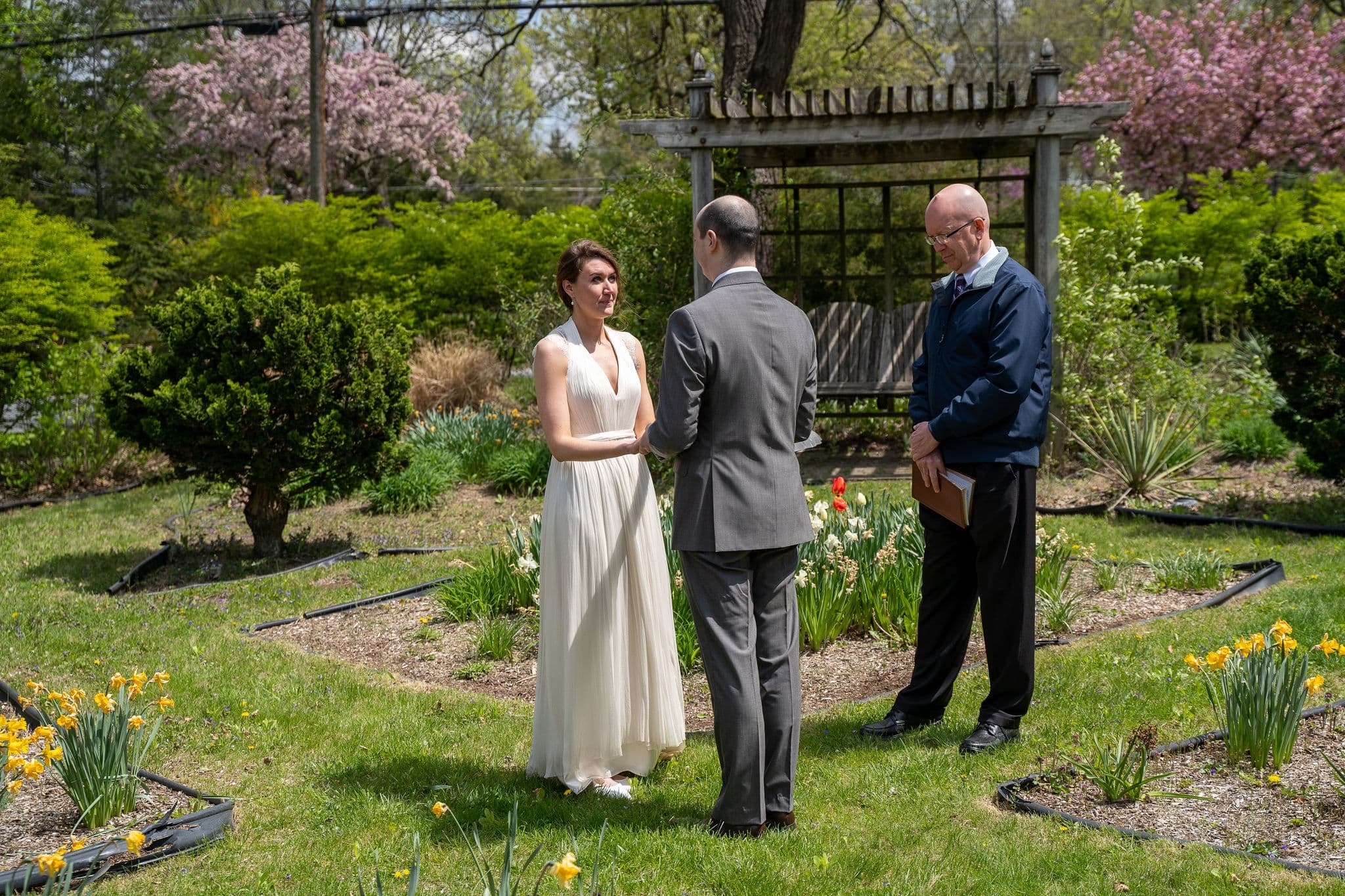 A couple exchanges vows in a garden while an officiant presides over their wedding ceremony.