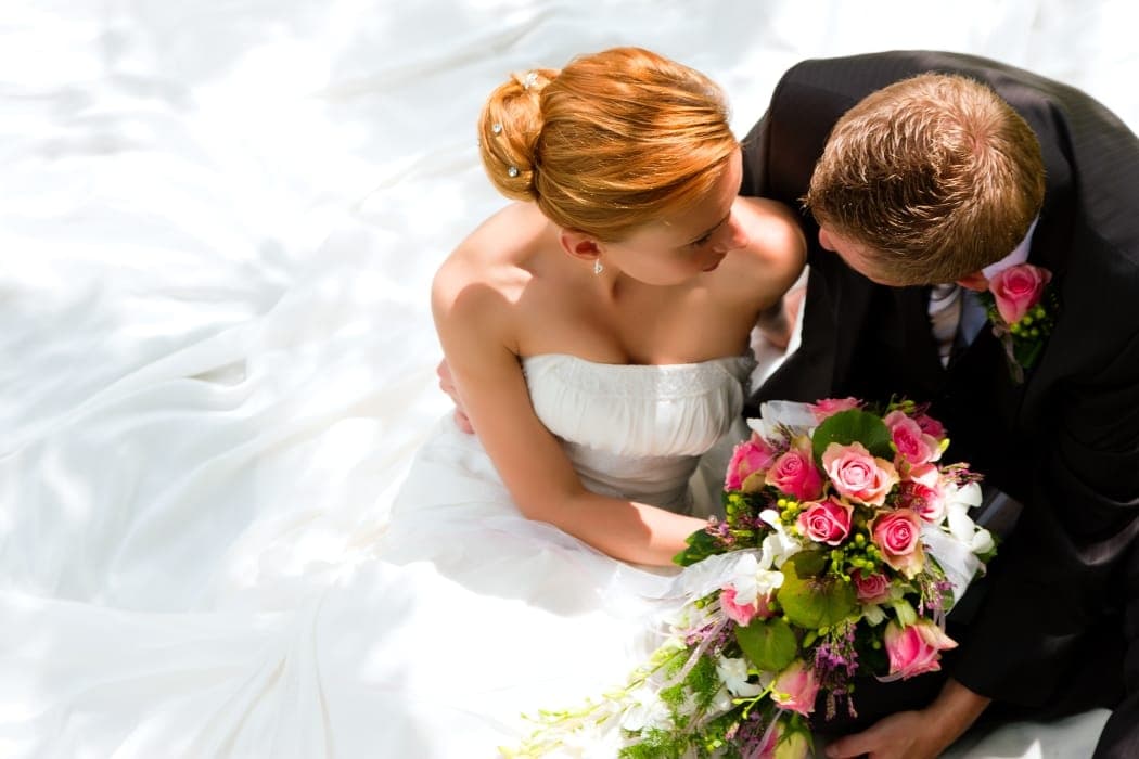 A bride and groom share an intimate moment, surrounded by a cascade of white fabric and vibrant flowers.